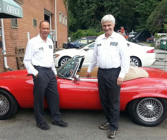 Owners standing outside of the job next to a red Jaguar.